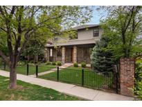 Charming two-story home with a well-manicured front yard, a black metal fence, and mature trees at 1927 S Grant St, Denver, CO 80210