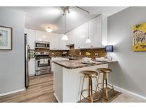 Updated kitchen with white cabinets, breakfast bar and stools, stainless steel appliances, and modern lighting at 710 S Clinton St # 3A, Denver, CO 80247