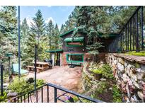Charming cabin exterior featuring a stone patio, outdoor dining, and lush landscaping at 5672 Santa Clara Rd, Indian Hills, CO 80454