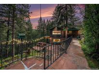 Charming cabin exterior with stone walkway, inviting patio, and lush green surroundings at twilight at 5672 Santa Clara Rd, Indian Hills, CO 80454