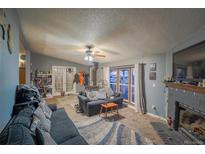 Cozy living room featuring a fireplace, ceiling fan, and ample natural light from large windows at 15682 Morris Ave, Fort Lupton, CO 80621
