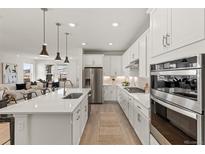 Modern kitchen features white cabinetry, stainless steel appliances, and an island with pendant lighting at 17412 W 93Rd Pl, Arvada, CO 80007