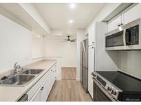 Modern kitchen features stainless steel appliances, white cabinets and light countertops; open to dining area with wood floors at 1113 W 112Th Ave # B, Denver, CO 80234