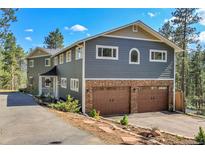 Two-story home with a stone-clad garage and gray siding, surrounded by trees and a blue sky at 4574 Picutis Rd, Indian Hills, CO 80454