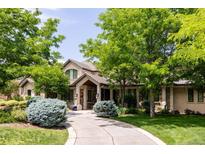 Stately stone home with lush landscaping, mature trees, and a curved driveway leading to the entrance at 4041 E Forbes Ct, Greenwood Village, CO 80121