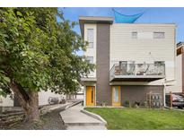 Modern townhome featuring a brick facade, balcony, well-kept lawn, and yellow entry door at 1711 Hooker St # 2, Denver, CO 80204