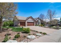 Charming brick home boasts a three-car garage and beautifully landscaped front yard on a sunny day at 4532 Christensen Cir, Littleton, CO 80123