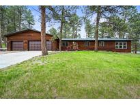 Charming wood home with a lush green lawn and a two-car attached garage surrounded by mature trees at 26499 West St, Conifer, CO 80433