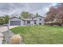 Charming gray home with a lush green lawn, mature trees, and an attached two-car garage at 1641 S Parfet Ct, Denver, CO 80232