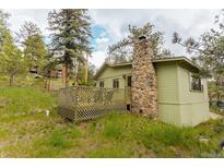 Side view of the home with wood siding, a stone chimney, and a partially fenced in patio area at 4850 Forest Hill Rd, Evergreen, CO 80439