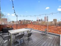 Charming rooftop patio with city views, string lights, table and chairs on a wood surface and brick wall at 1130 N N Pennsylvania St # 306, Denver, CO 80203