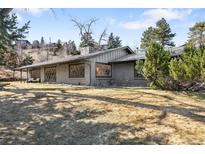 A single story home with light grey brick, diamond grid windows and mature trees at 14475 Foothill Rd, Golden, CO 80401