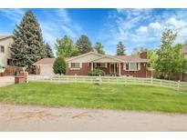 Charming red brick home featuring a well-manicured lawn, white picket fence and mature trees at 1160 Johnson St, Lakewood, CO 80215