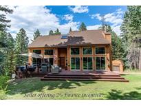 Charming exterior features a spacious deck, large windows, and an American flag, blending seamlessly into the surrounding landscape at 25257 Snyder Ave, Conifer, CO 80433