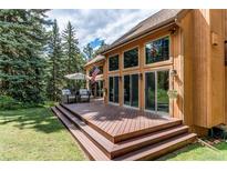 Beautiful home featuring a large wooden deck with ample seating overlooking a well-manicured lawn at 25257 Snyder Ave, Conifer, CO 80433