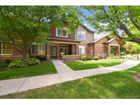 Inviting exterior of brick home featuring a covered porch, mature trees, and manicured lawn at 6404 Silver Mesa Dr # E, Highlands Ranch, CO 80130