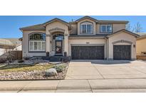 Two-story stucco home showcasing an attached three car garage, a manicured lawn and a stone walkway up to the front door at 10472 Grizzly Gulch, Highlands Ranch, CO 80129