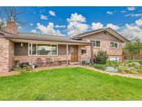Charming brick home features a covered porch with seating and a lush, green lawn at 55 S Flower St, Lakewood, CO 80226