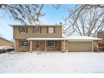 Charming two-story home with brick accents, a covered porch, and a two car garage, all dusted with snow at 360 S 30Th Ave, Brighton, CO 80601