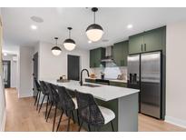 Bright kitchen showcasing a large island with bar seating, matte green cabinets, stainless appliances, and hardwood floors at 3275 Lawrence St, Denver, CO 80205