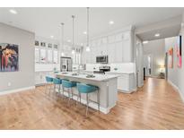 Bright kitchen featuring white cabinets, a large island with bar seating, and pendant lighting over light wood-look floors at 17720 W 94Th Dr, Arvada, CO 80007