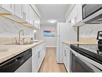 Bright kitchen features white cabinets, stone countertops, stainless steel sink and appliances, and wood-look flooring at 7645 E Quincy Ave # 105, Denver, CO 80237