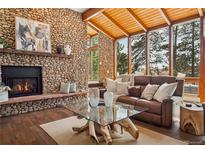 Inviting living room features a stone fireplace, wood ceiling, and large windows offering views of the surrounding landscape at 31607 Broadmoor Dr, Evergreen, CO 80439