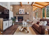 Cozy living room with stone fireplace, wood ceiling beams, and expansive windows offering natural light at 31607 Broadmoor Dr, Evergreen, CO 80439