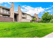 Exterior view of condos with stone chimneys, wood siding, and well-manicured lawn and blue sky at 7750 W 87Th Dr # C, Arvada, CO 80005