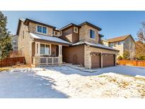 Inviting two-story home featuring a three-car garage and a cozy front porch in a winter landscape at 8850 W Cannes Dr, Littleton, CO 80127