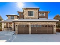 Beautiful two-story home featuring a stone facade, two-car garage, and charming front porch in a snowy landscape at 8850 W Cannes Dr, Littleton, CO 80127