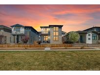 Modern two-story home with stone accents, balcony, fenced yard, and a vibrant sunset backdrop at 6054 N Perth St, Aurora, CO 80019