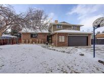 Two-story home with a brick and brown siding, attached garage, and snow-covered front yard at 7835 Nelson St, Arvada, CO 80005