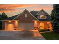 Charming brick home with a three-car garage illuminated by warm exterior lights and a beautiful sunset at 7472 S Utica St, Littleton, CO 80128
