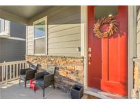 Charming front porch features stone accents, cozy seating, and a vibrant red door with wreath at 17397 Red Cosmos Pt, Parker, CO 80134