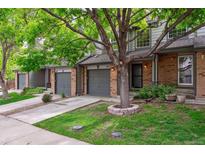 Charming townhome featuring brick accents, a gray garage door, and a well-manicured lawn with a mature shade tree at 1953 E 102Nd Cir, Thornton, CO 80229