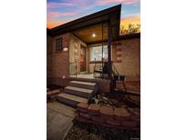 Charming brick home showcasing a cozy covered front porch with wrought iron details at twilight at 2042 Jamaica St, Aurora, CO 80010