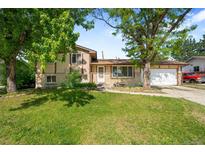 A well-kept lawn complements this charming two-story home with mature trees and a welcoming front entrance at 6953 Ingalls St, Arvada, CO 80003
