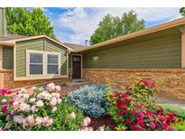 Charming front entrance featuring a well-maintained garden with colorful flowers and brick accents at 13849 W 66Th Dr, Arvada, CO 80004