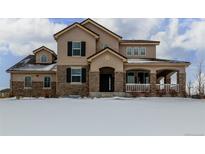 Charming two-story home featuring stone accents and a welcoming front porch and snow covered yard at 42280 Kingsmill Cir, Elizabeth, CO 80107