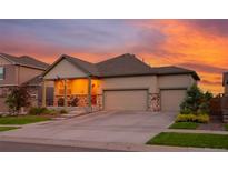 Charming home with a two-car garage, covered porch, stone accents, and beautiful landscaping during sunset at 19468 E 65Th Pl, Aurora, CO 80019
