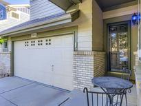 Home exterior with a two-car garage, brick details, front door, and small outdoor seating area at 11811 Lewiston St, Commerce City, CO 80022