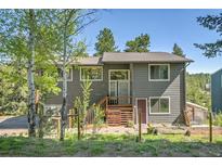 Charming gray two-story home with a wooden deck and a small garden, surrounded by lush greenery and tall trees at 30273 Conifer Rd, Evergreen, CO 80439