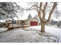 Charming home featuring a spacious wooden deck, red garage door and snow-covered front yard with mature trees at 4274 S Fundy Way, Aurora, CO 80013