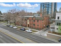 Three-story brick apartment building on a tree lined street with parked cars and a tall building in the background at 3132 E 17Th Ave # B, Denver, CO 80206