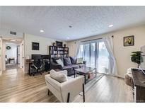Bright living room with wood floors, a comfortable sofa, bookshelf, work area, and sliding doors to the outside at 12131 Melody Dr # 201, Denver, CO 80234
