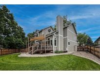 Charming home with a backyard featuring a wooden deck, lush lawn, and mature trees against a blue sky at 6255 Collegiate Dr, Highlands Ranch, CO 80130