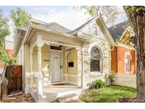 Charming yellow home featuring an inviting front porch with decorative white railings and a well-manicured lawn at 2909 Glenarm Pl, Denver, CO 80205