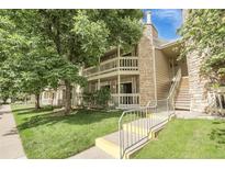Inviting two-story condo featuring a charming balcony, stone accents, and lush green landscaping at 8225 Fairmount Dr # 102, Denver, CO 80247