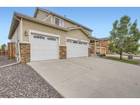Home exterior featuring a three-car garage, concrete driveway, stone accents, and well-maintained landscaping at 56579 E 23Rd Pl, Strasburg, CO 80136